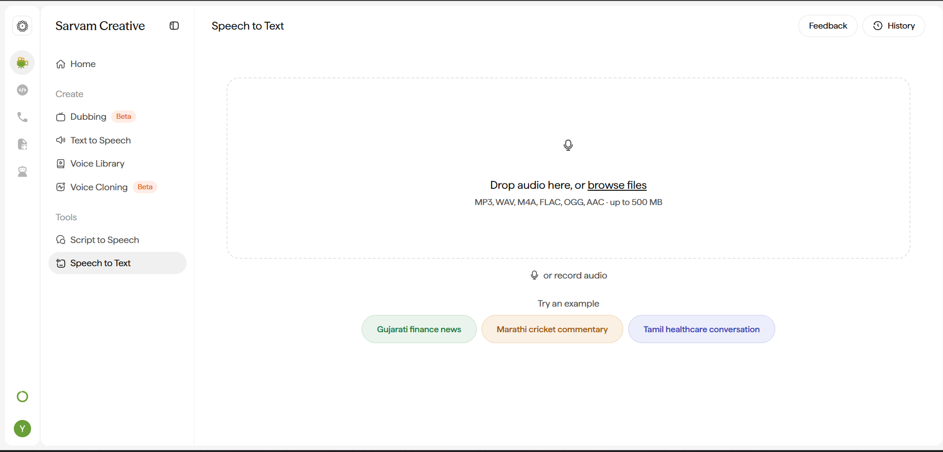 Speech to Text screen. Header has Feedback and History buttons. The main panel is a dashed-border drop zone with a microphone icon reading Drop audio here, or browse files, with the caption listing supported formats and a 500 MB size limit. Below it, a second option reads or record audio with its own microphone icon. Below that, Try an example offers three colored example chips: Gujarati finance news, Marathi cricket commentary, and Tamil healthcare conversation.