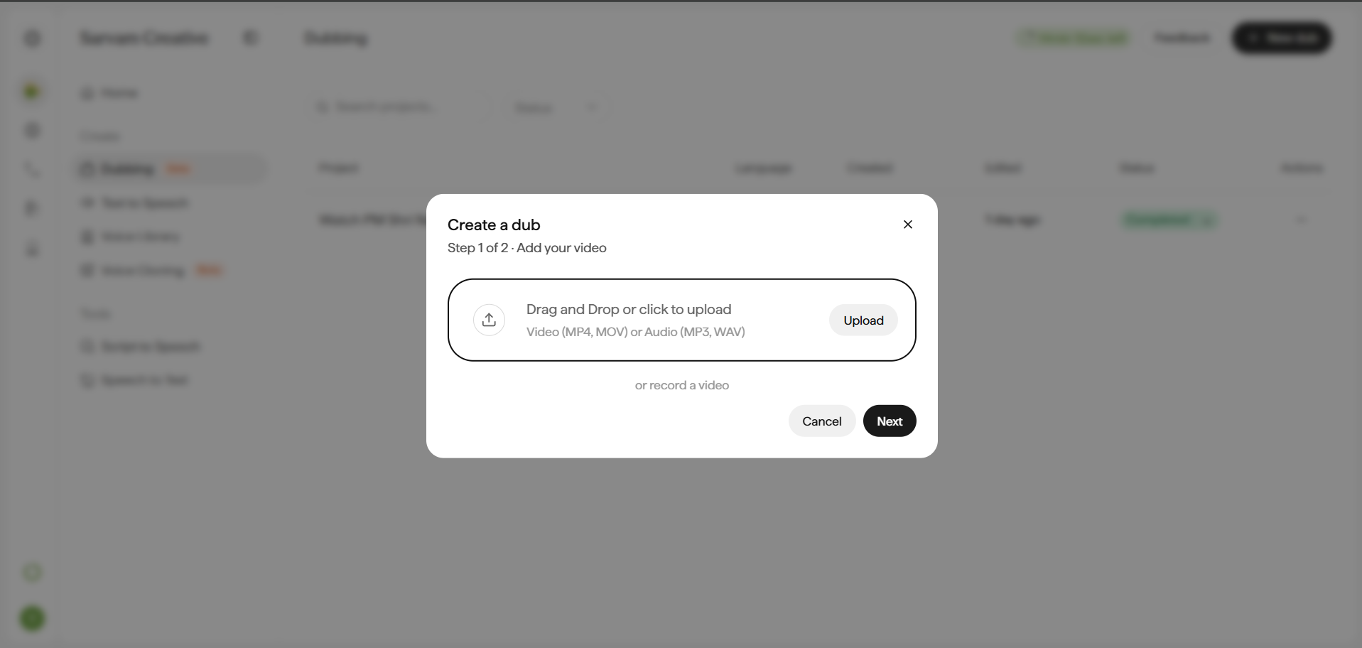 Create a dub modal, Step 1 of 2, titled Add your video, shown over a blurred background list of past dub projects. A bordered dropzone reads Drag and Drop or click to upload, with the caption Video (MP4, MOV) or Audio (MP3, WAV) and an Upload button on the right. Below the dropzone, a text link reads or record a video. The modal footer has Cancel and Next buttons.